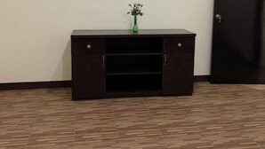 A room with a dark wooden cabinet, a small green vase with flowers, and a closed black door. - Carolina Townhome (Catanauan)