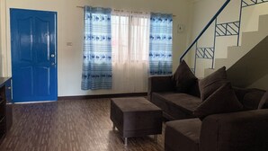 A living room with a blue door, a sofa set, a wooden floor, and a staircase. - Carolina Townhome (Catanauan)
