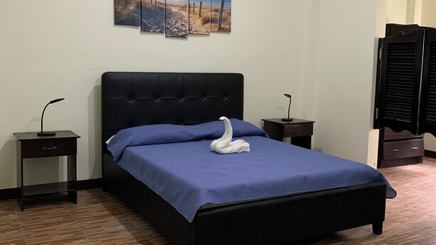 A bedroom with a bed, a nightstand, a wall-mounted TV, and a painting. - Carolina Townhome (Catanauan)