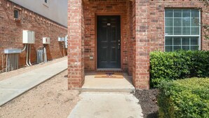 A brick building with a black door, a small window, and a doormat with "Texas Tech" on it. - Convenient Condo - 2BR 2 BA - Walk to Tech (Lubbock)