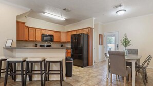 A modern kitchen with wooden cabinets, a black refrigerator, and a bar area with stools. - Convenient Condo - 2BR 2 BA - Walk to Tech (Lubbock)