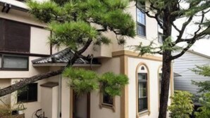 A building with a traditional architectural style, featuring a prominent tree in the foreground and a bicycle parked against the wall. - Rakumankan (Kyoto)