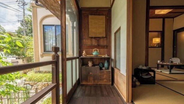 A narrow wooden corridor with a tatami mat room on the right, a window on the left, and a view of greenery outside. - Rakumankan (Kyoto)