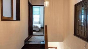 A narrow hallway with a wooden floor, a bed in the background, and a hanging light fixture. - Rakumankan (Kyoto)