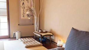 A traditional Japanese room with tatami flooring, a low table with a tray, a cushion, and a hanging scroll. - Rakumankan (Kyoto)