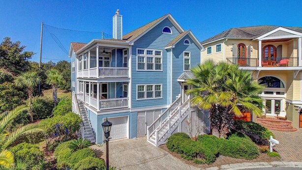A two-story house with a balcony, a garage, and a well-maintained garden with palm trees. - Palmetto Moon | Ocean Point Retreat near Beach, Pool & Golf (Isle of Palms)