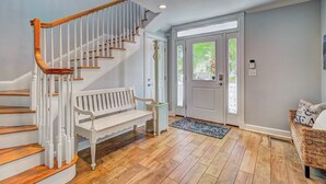 A staircase with wooden handrails and white steps, a white bench, a door with glass panels, and a wicker basket with cushions. - Palmetto Moon | Ocean Point Retreat near Beach, Pool & Golf (Isle of Palms)