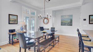 A dining room with a glass table, dark chairs, and a chandelier. - Palmetto Moon | Ocean Point Retreat near Beach, Pool & Golf (Isle of Palms)