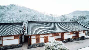 A traditional Japanese building with a tiled roof and wooden walls, surrounded by snow-covered trees and hills.
