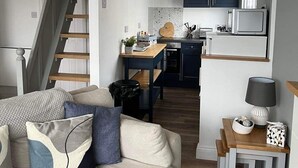 A compact living space with a sofa, a dining table, a kitchen area with dark cabinets and a microwave, and a staircase leading to another level. - Seasideescape-2br-sleeps4-parking-petsok-fireplace (Bridlington)