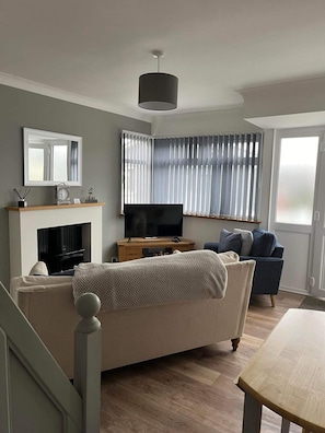 A living room with a fireplace, a television, a sofa, and a dining table. - Seasideescape-2br-sleeps4-parking-petsok-fireplace (Bridlington)