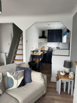 A compact living space with a kitchenette, a sofa with cushions, a dining table, and a staircase.