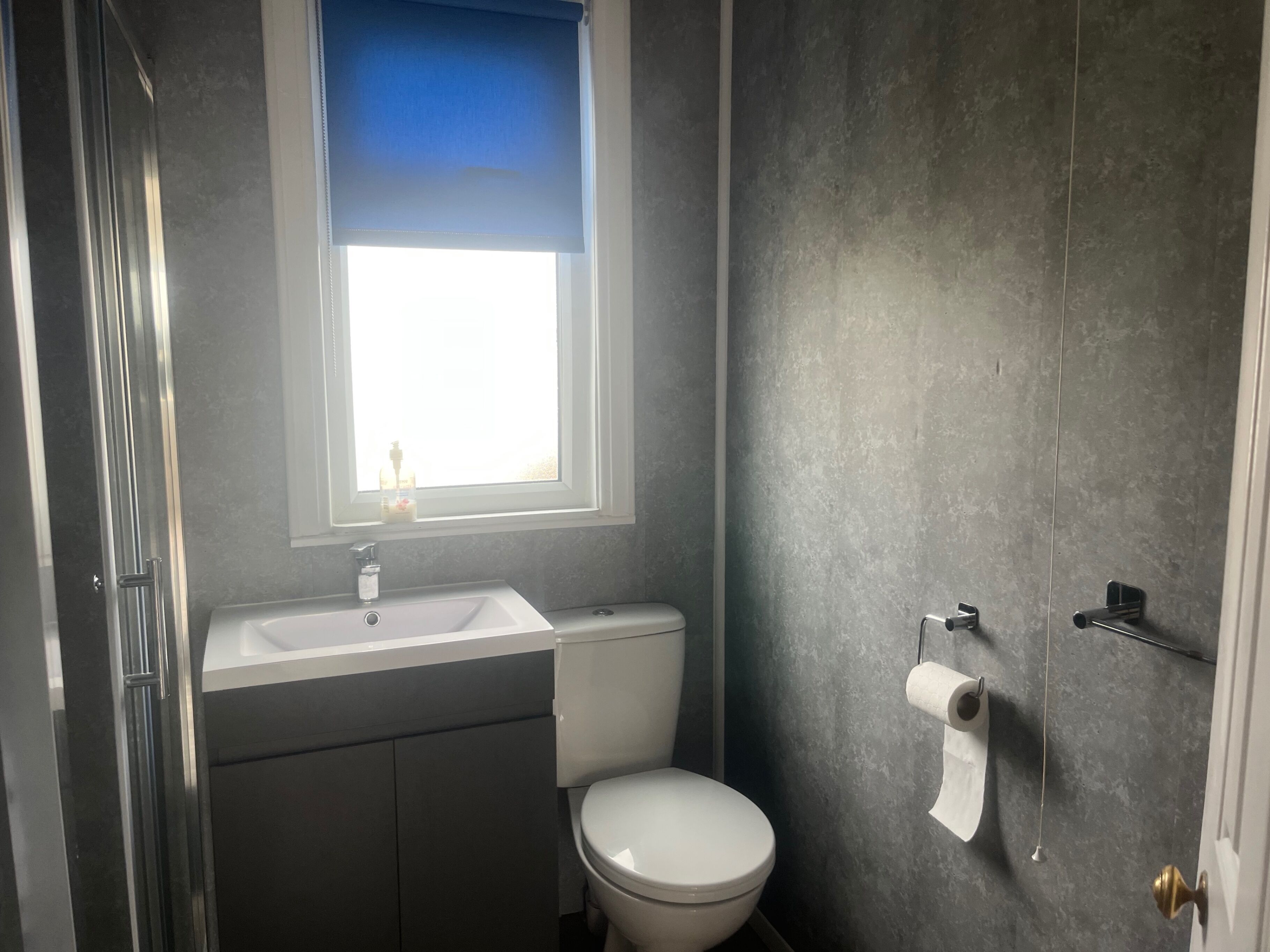 A bathroom with a white toilet, a sink, and a window with a blue blind.