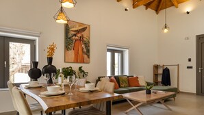 A modern dining area with a wooden table set for four, surrounded by chairs. A painting of a woman in traditional attire hangs on the wall. - Casa Dionysia (Platanias)