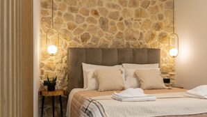 A bedroom with a stone wall, a tufted headboard, and two bedside lamps. - Casa Dionysia (Platanias)
