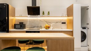 A modern kitchen with a marble countertop, a built-in microwave, a sink, and a washing machine. There are two green bar stools and two potted plants on the countertop. - Casa Dionysia (Platanias)