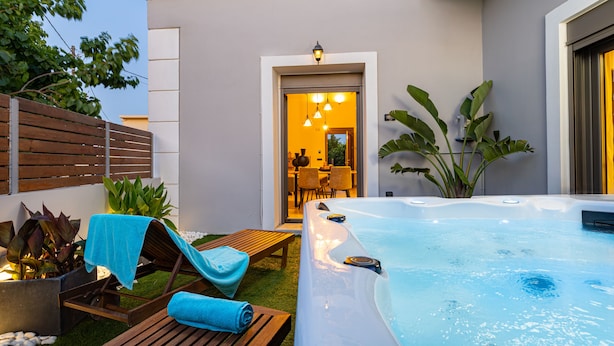 A hot tub with a wooden deck and lounge chairs, a dining area with chairs and a table, and a large plant. - Casa Dionysia (Platanias)