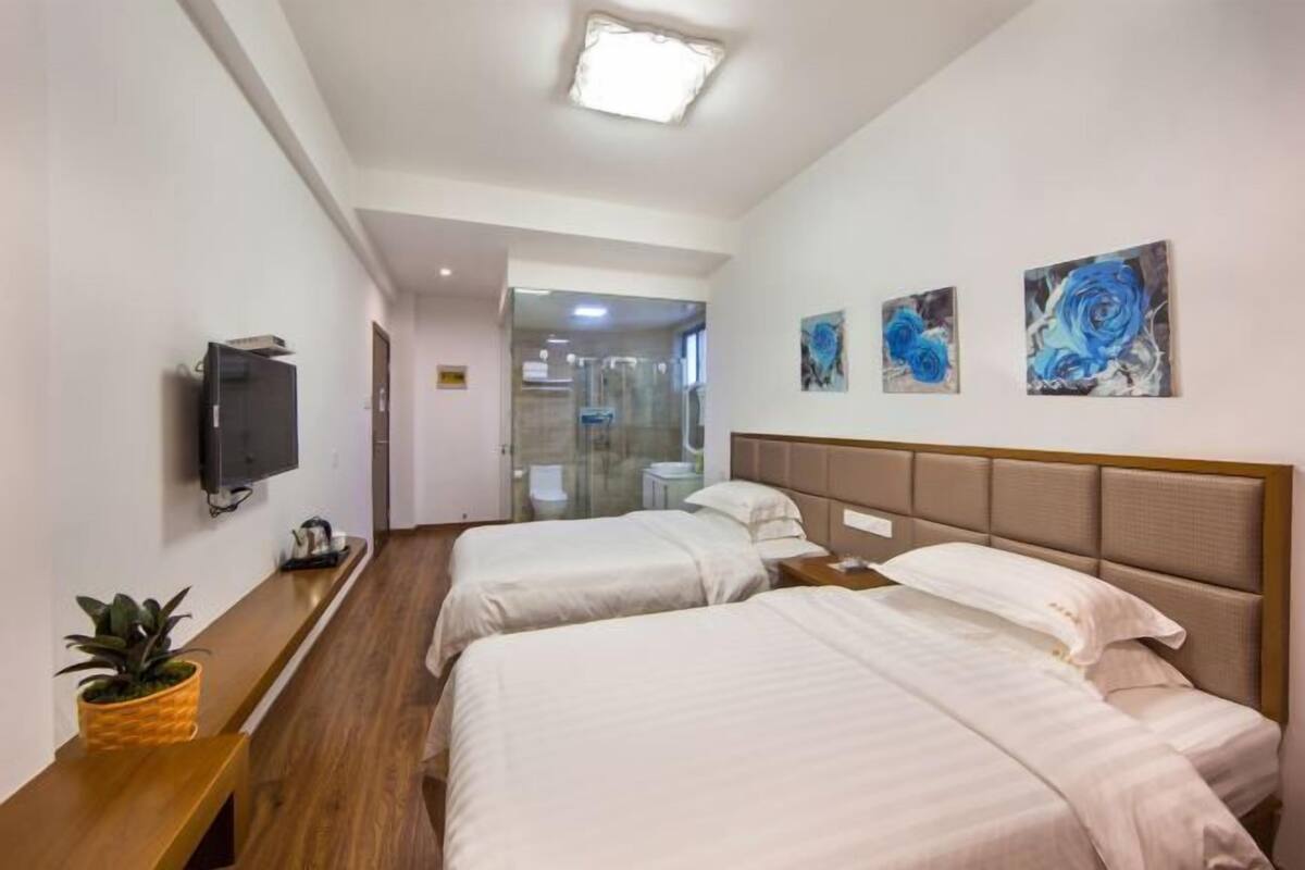 A hotel room with two beds, a TV, artwork on the wall, and a wooden bench.
