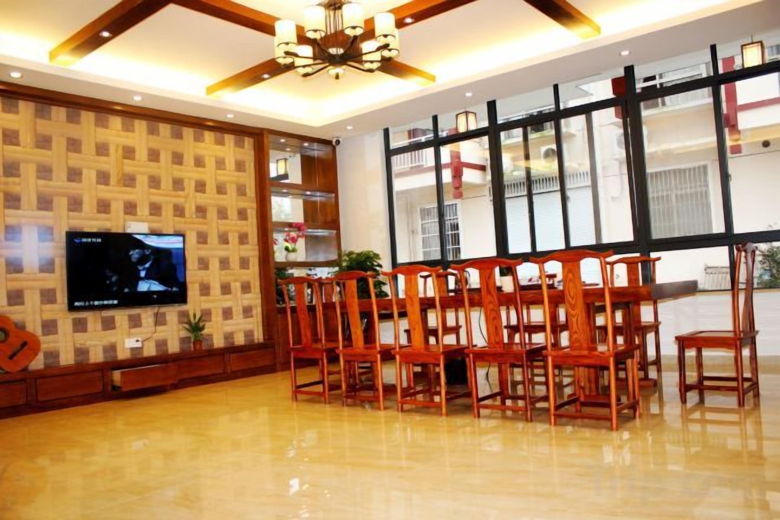 A dining area with a wooden table and chairs, a television on the wall, and a large window with a view of the outside.
