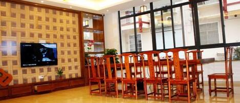A dining area with a wooden table and chairs, a television on the wall, and a large window with a view of the outside.