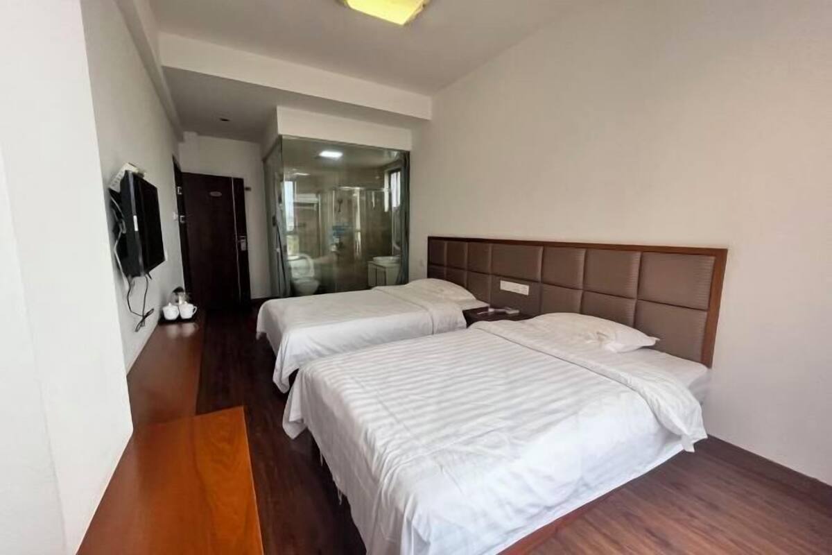 A hotel room with two beds, a television, and a bathroom visible through a glass door.