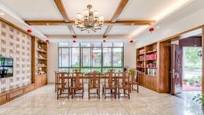 A spacious room with a dining table, chairs, a chandelier, and large windows. - Hengyou Hostel (Wuyishan)