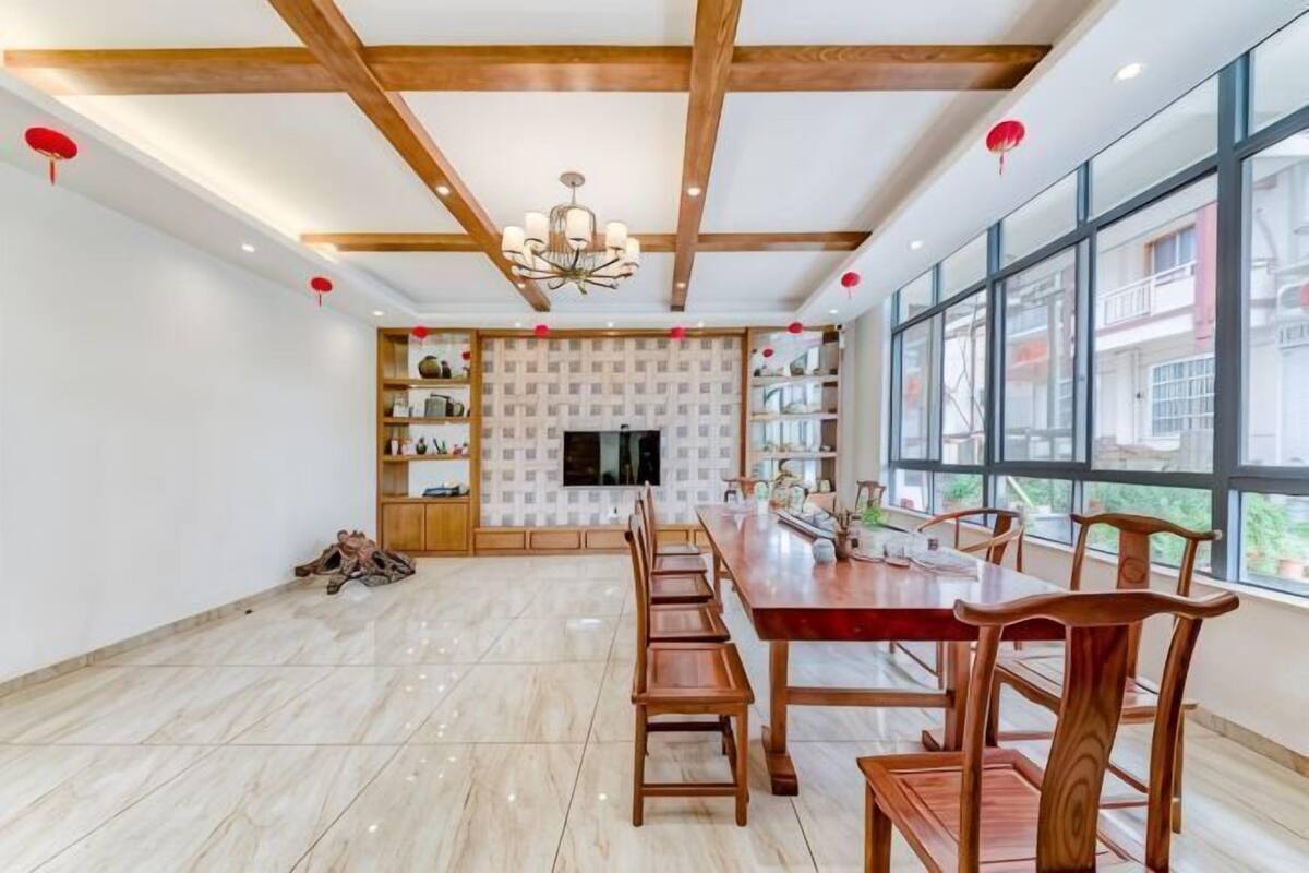 A spacious dining area with a long wooden table and chairs, a chandelier, and large windows.