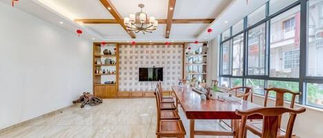 A spacious room with a long dining table, wooden chairs, a chandelier, and large windows.