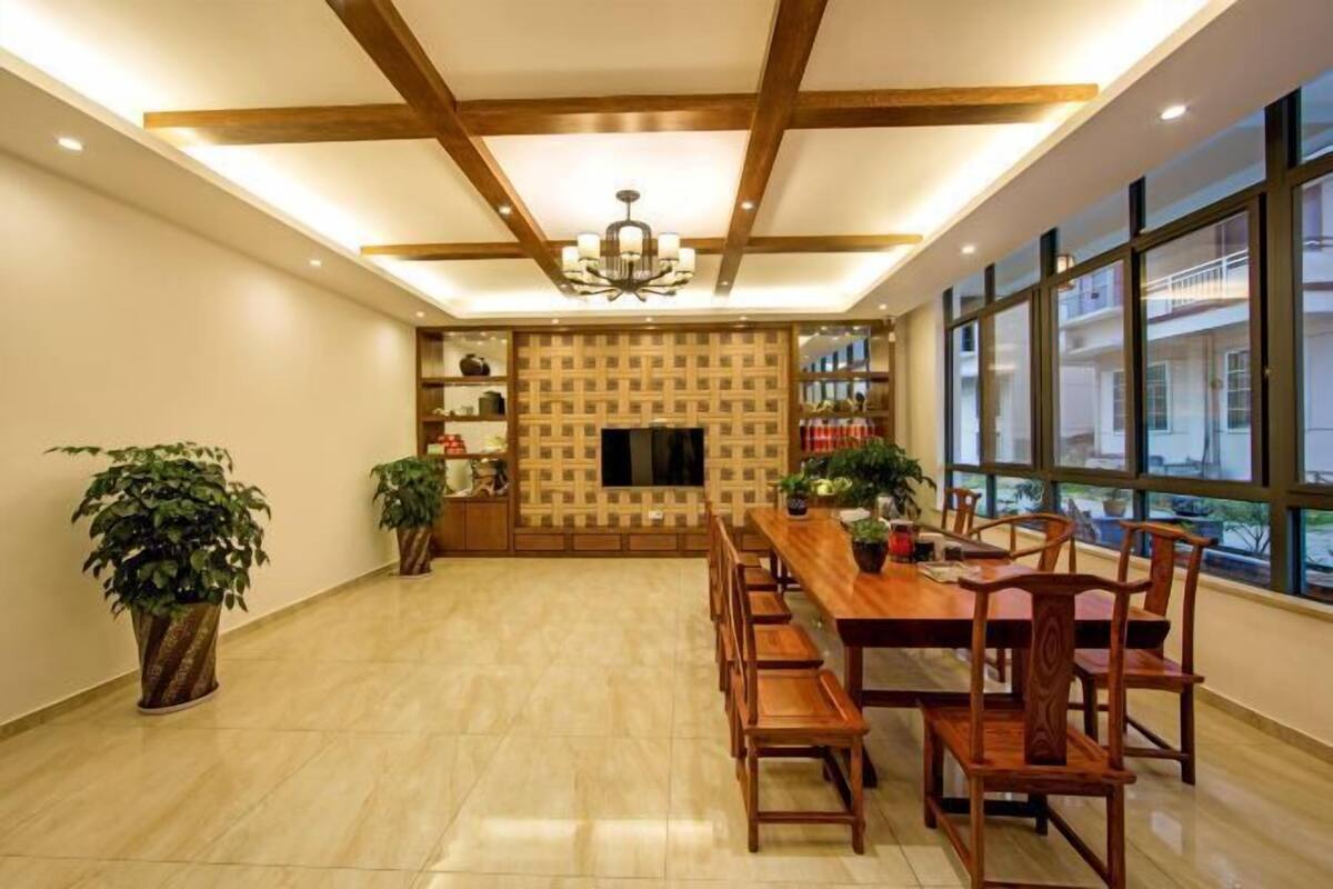 A dining area with a wooden table, chairs, potted plants, a chandelier, and a TV screen.