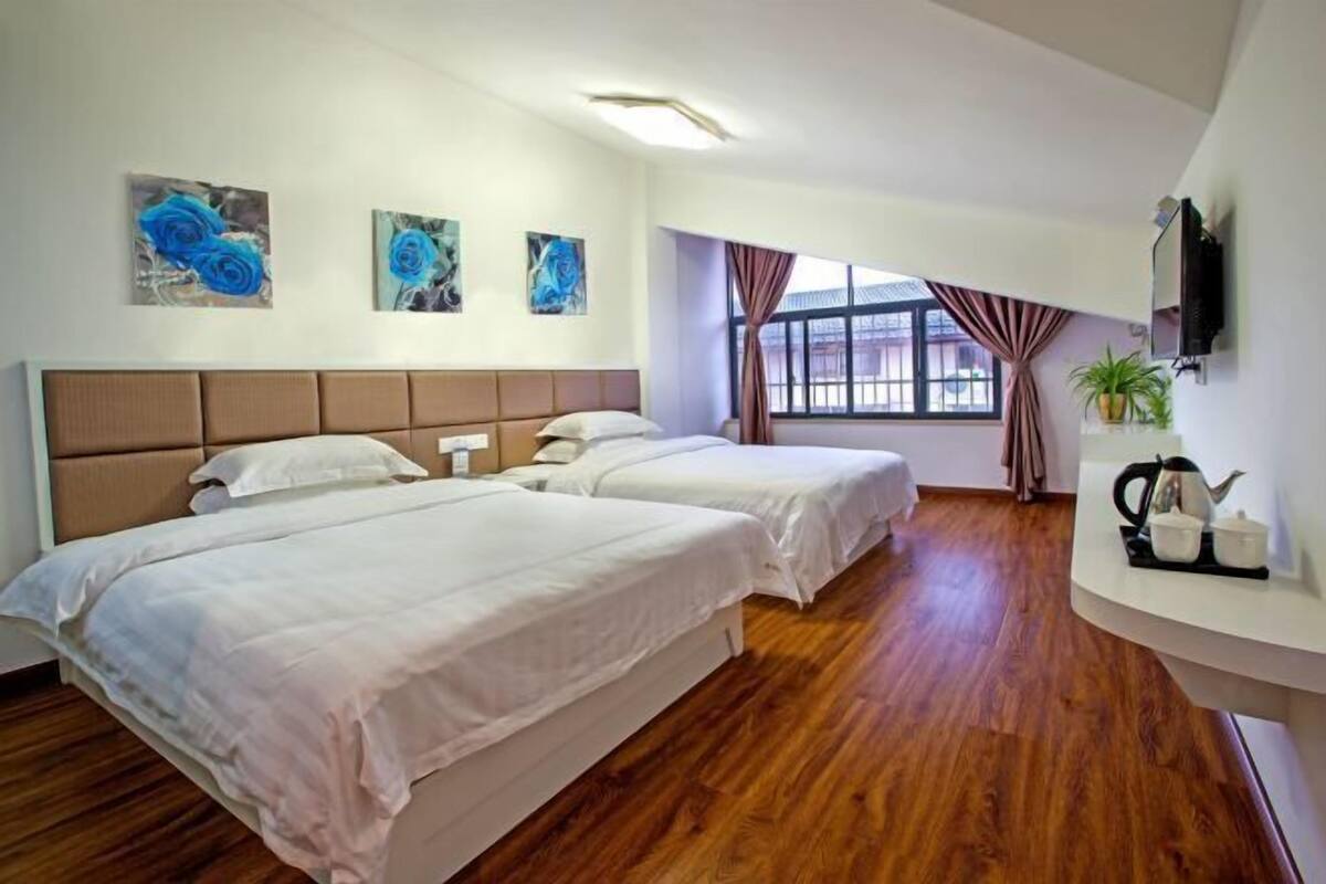 A hotel room with two beds, a TV, a window with curtains, and artwork on the wall.