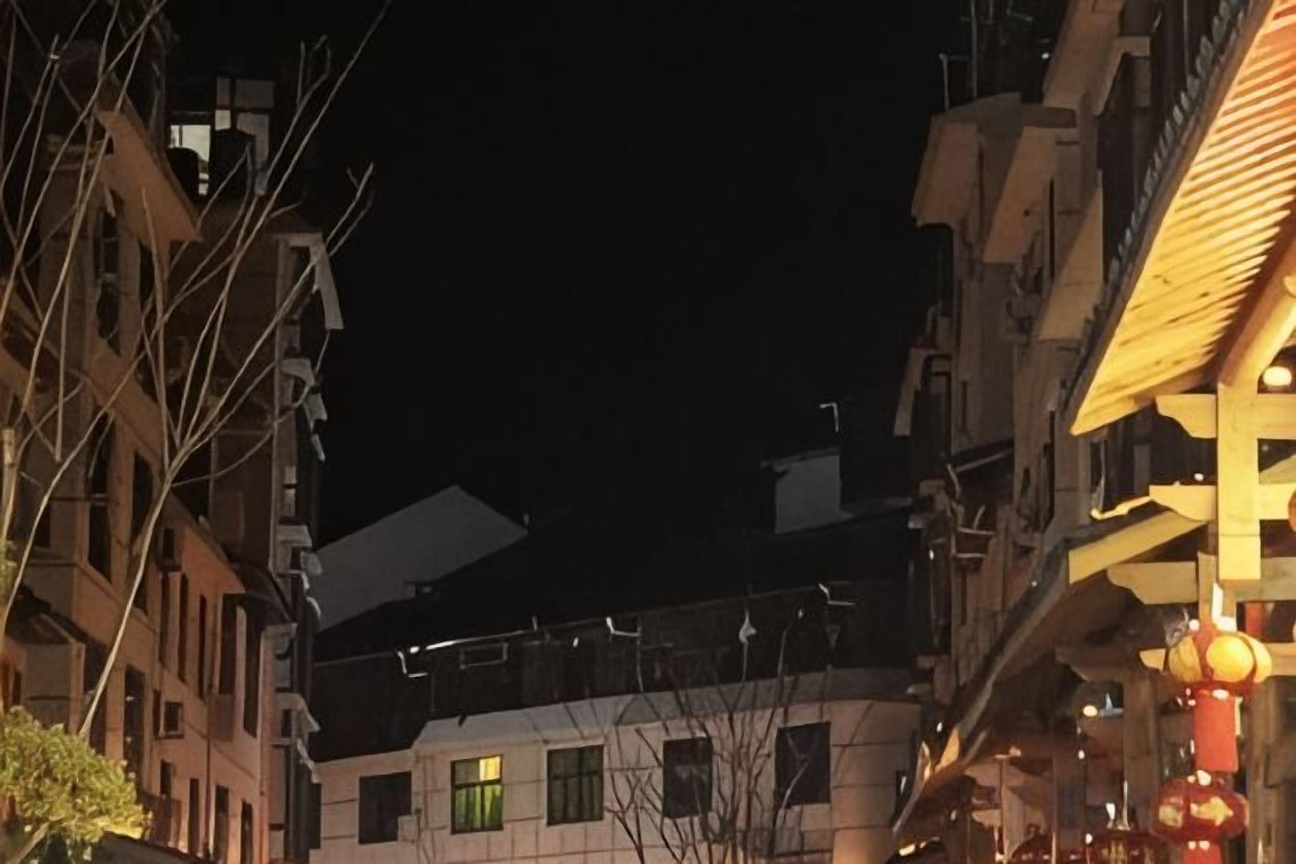 Vista nocturna de un edificio de varios pisos con balcones e iluminado en una esquina.