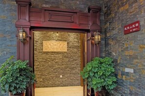 A hotel entrance with a stone wall, wooden door frame, and two potted plants. - Hengyou Hostel (Wuyishan)