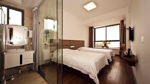 A hotel room with a glass shower enclosure, a white vanity, two beds with white linens, a large window with curtains, and a flat-screen TV mounted on the wall. - Hengyou Hostel (Wuyishan)