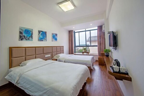 A hotel room with two beds, a wooden headboard, a large window with curtains, and a TV mounted on the wall. - Hengyou Hostel (Wuyishan)