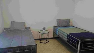 Una habitación pequeña y sencilla con dos camas, una mesita y una lámpara en el techo.