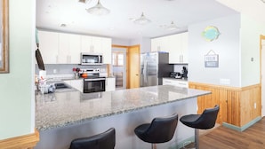 Una cocina moderna con encimeras de granito, electrodomésticos de acero inoxidable y una isla central con taburetes de bar.