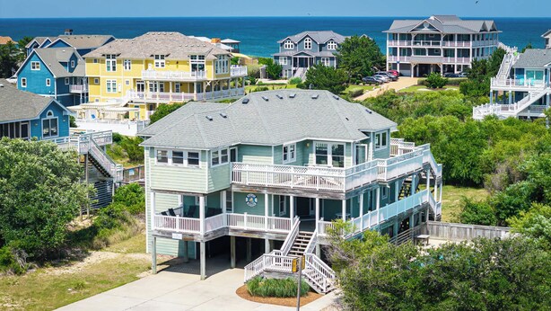 Una casa frente al mar con varios balcones, un porche delantero y una escalera que conduce al nivel superior.
