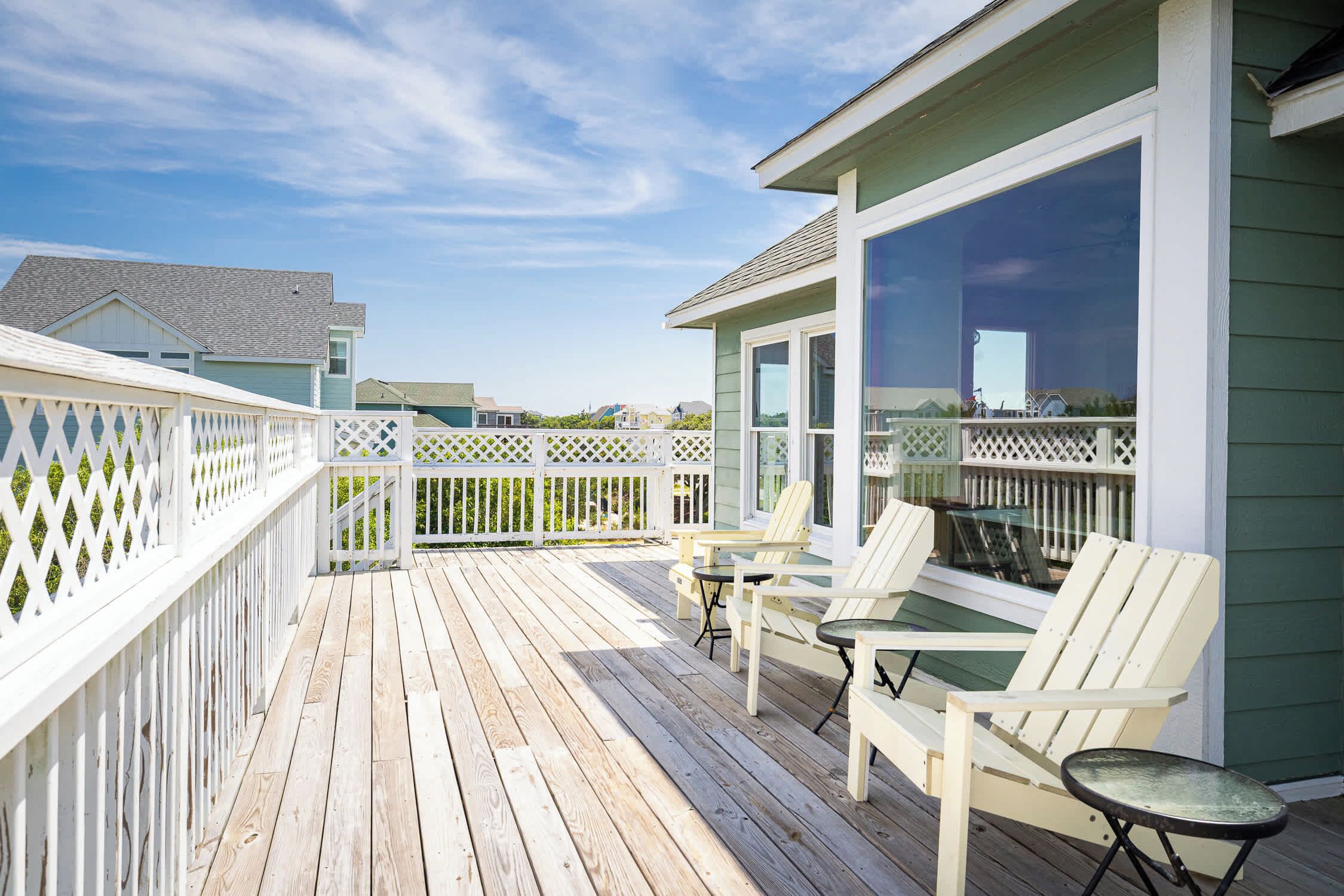 A wooden deck with white railings, a glass door, and two Adirondack chairs.