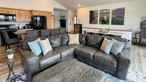 Un salon moderne avec un canapé d’angle en cuir, un coin repas et une cuisine dotée de meubles en bois et d’un réfrigérateur noir.