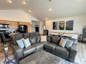 A modern living room with a leather sectional sofa, a dining area, and a kitchen with wooden cabinets and a black refrigerator. - Beach Cottage • Private Lake • Sleeps 14 (New Lisbon)