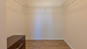 A small, empty room with a wooden floor, a metal ceiling rack, and a single wooden dresser. - Luxury Apt with Kitchen and Pool (Boston)