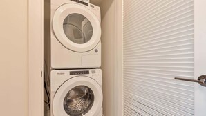 A stacked washer and dryer unit in a laundry room with a closed door in the background. - Luxury Apt with Kitchen and Pool (Boston)