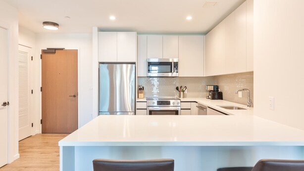 A modern kitchen with white cabinetry, stainless steel appliances, and a central island with bar stools. - Luxury Apt with Kitchen and Pool (Boston)