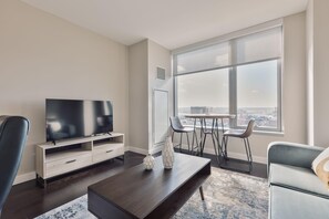Ett modernt vardagsrum med en stor TV, ett soffbord och utsikt över en stadssiluett genom stora fönster.