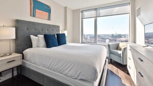 Ein modernes Hotelzimmer mit einem großen Bett, einem Schreibtisch und Blick auf die Stadt durch ein großes Fenster.