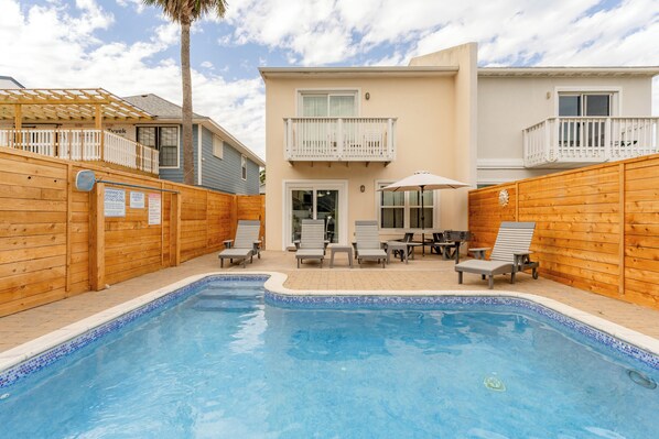 A swimming pool with lounge chairs and a wooden fence.