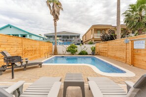 A swimming pool with lounge chairs, wooden fences, and a lifeguard sign.