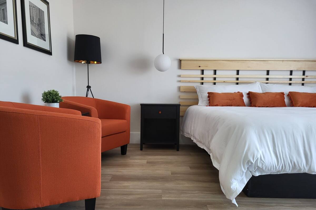 A bedroom with a bed, a nightstand, a lamp, a chair, and framed pictures on the wall.