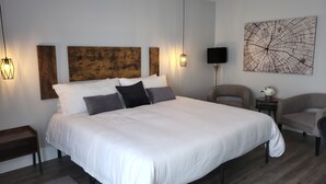 Ein modernes Schlafzimmer mit einem großen Bett, einem Holzkopfteil, zwei Wandleuchten, einem Nachttisch mit einer Vase und einem großen abstrakten Gemälde.