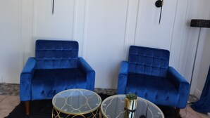 Ein Zimmer mit zwei blauen Samsofas, einem Glastisch mit goldener Zierleiste und zwei Wandlampen.